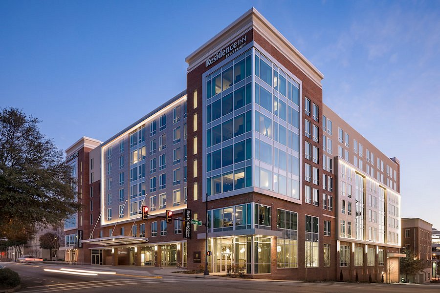 Photo of a multi-story brick hotel (approximately 7 stories). The photo was taken at an angle, so that the corner of the building is most prominent. This angle shows off the glass windows that create the corner and take up several stories of the hotel. It is nearly dusk.